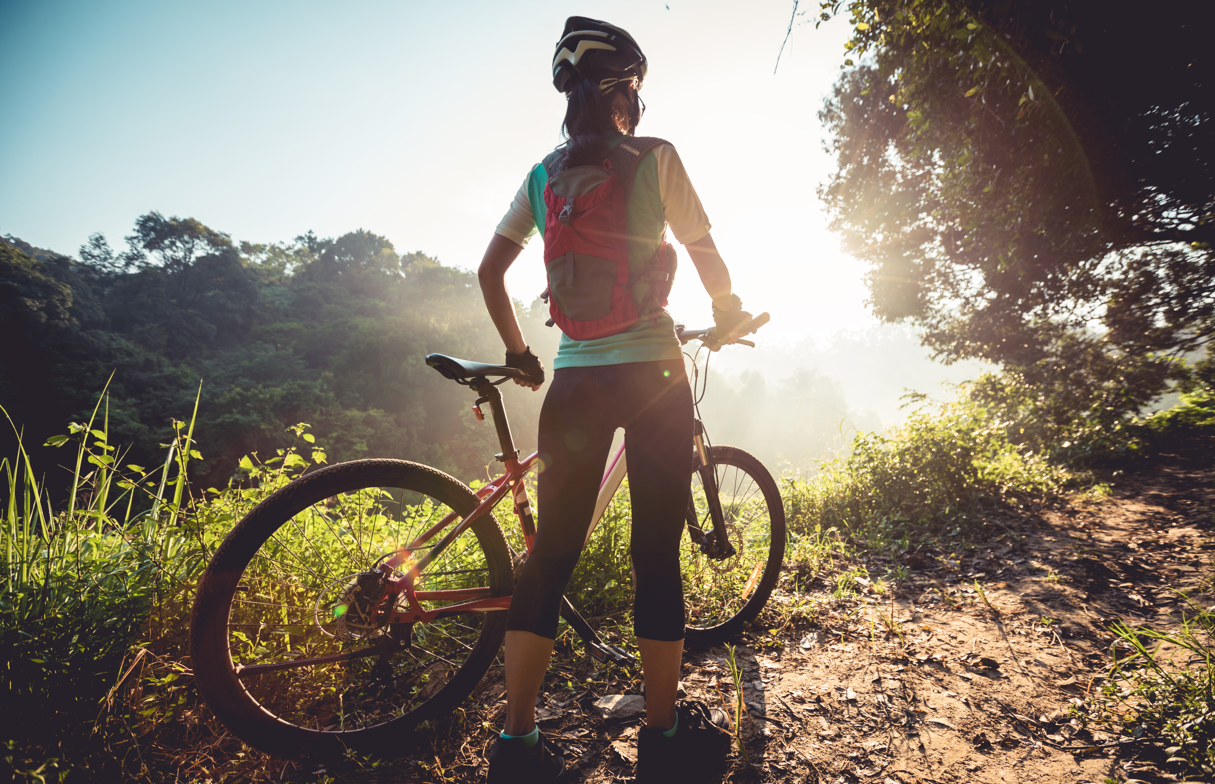 Woman standing beside bicycle looking out past the horizon