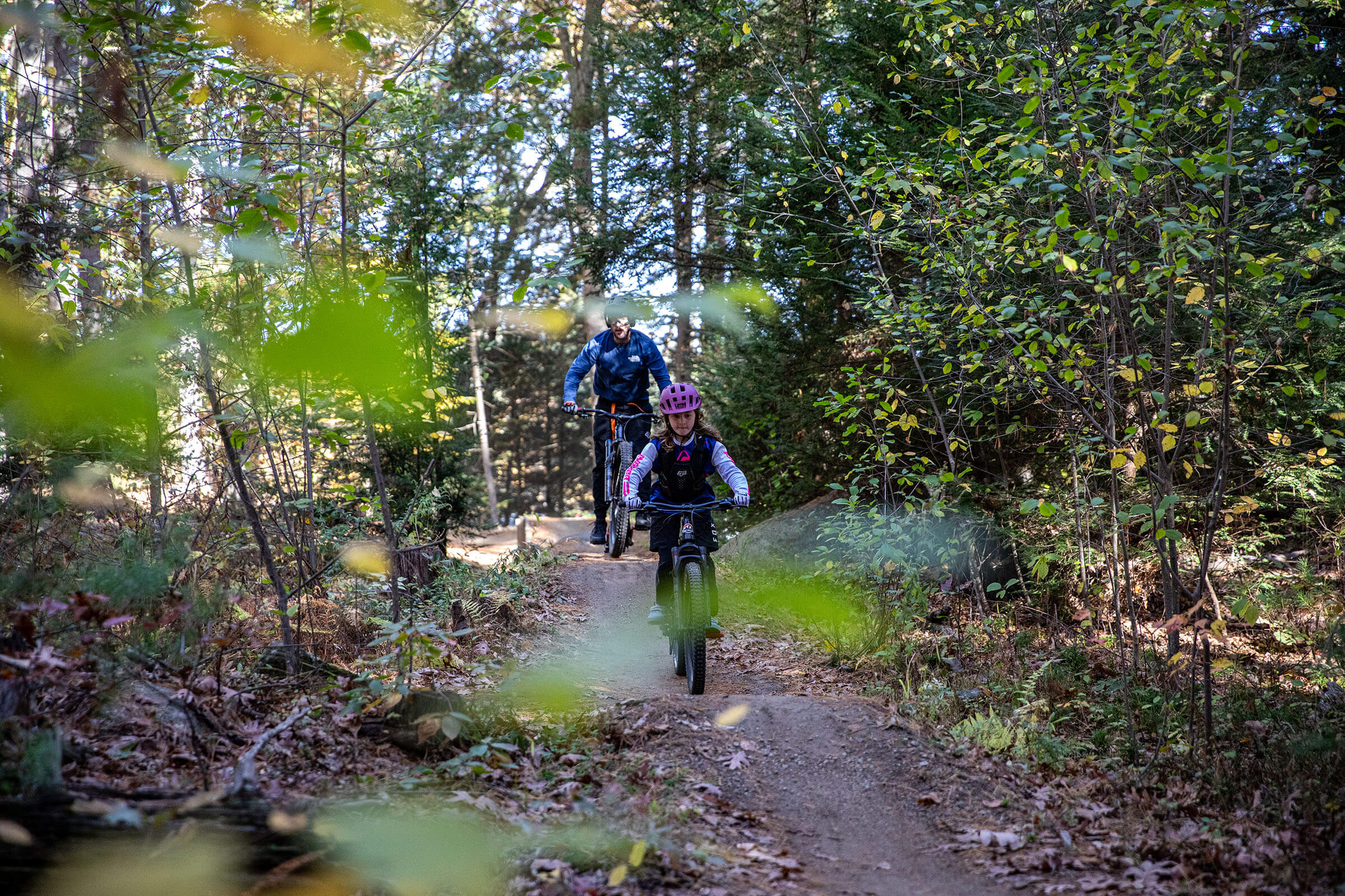 Man and girl mountain biking on a trail in the woods