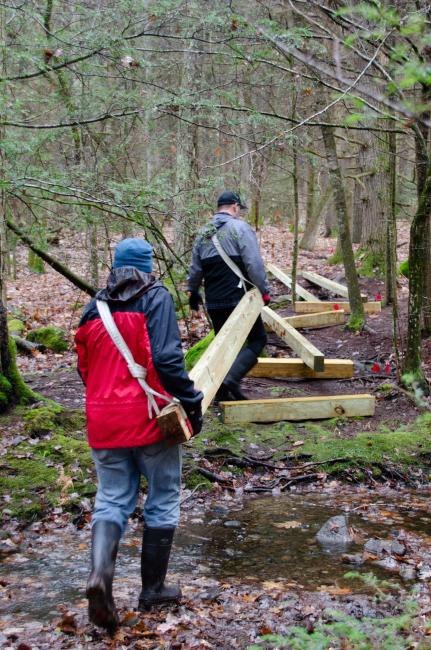 Photo of two people carrying large wooden board to construct raised wooden bike path.