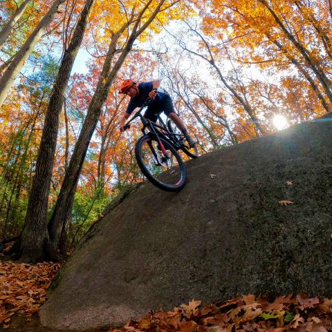 Photo of a cyclists riding their bike off a large rock.