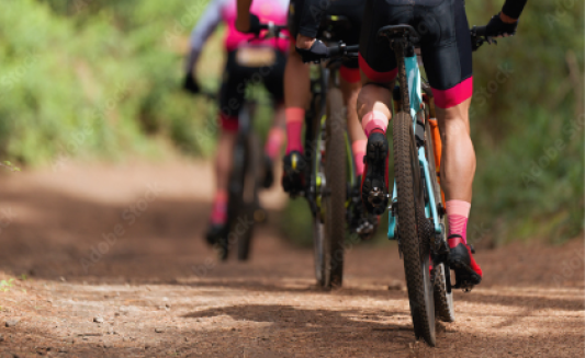 Image shows mountain bikers from the waist line down who are biking away from view on a dirt path.